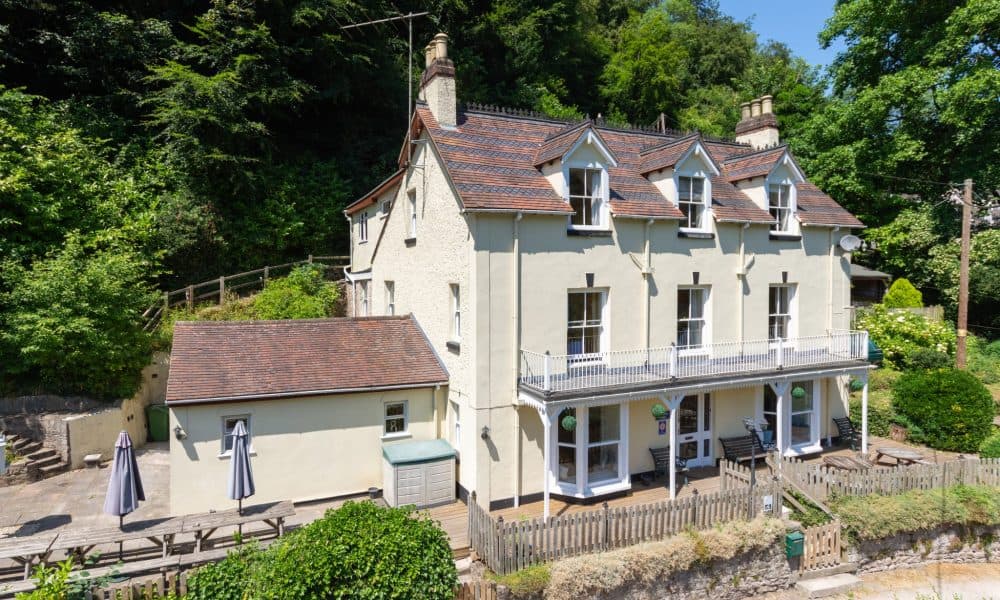 Cream Victorian mansion with slate roof and dormer windows surrounded by lush green trees