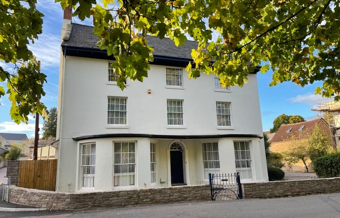 White-fronted Georgian period property with stone plinth, green foliage and blue sky