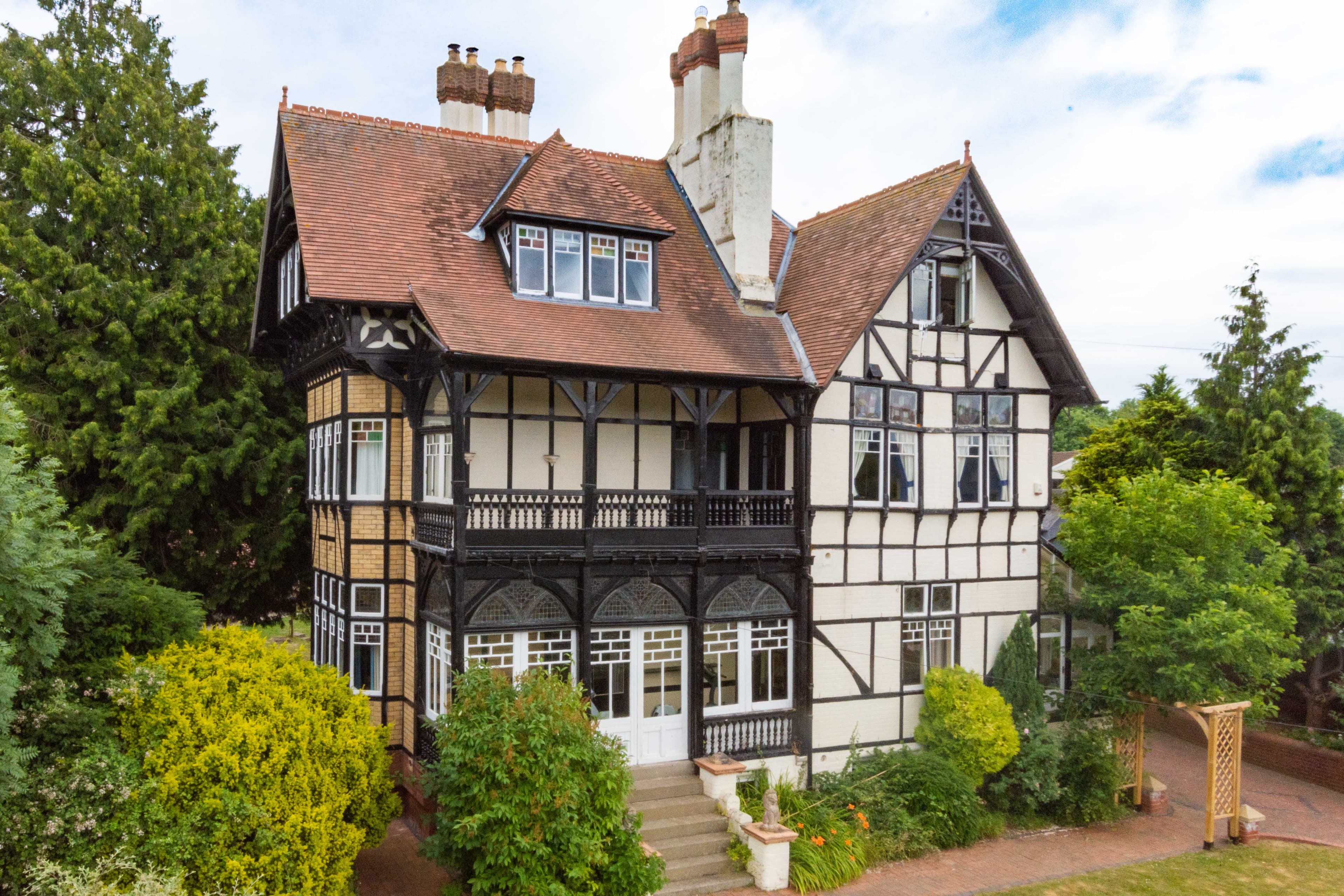 Half-timbered Tudor mansion with decorative balustrade, multiple chimneys, and manicured gardens