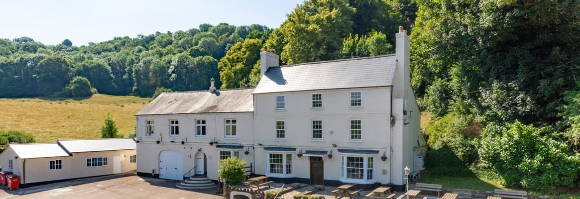 Large country manor with white rendered walls, slate roof, and adjoining buildings in rural setting