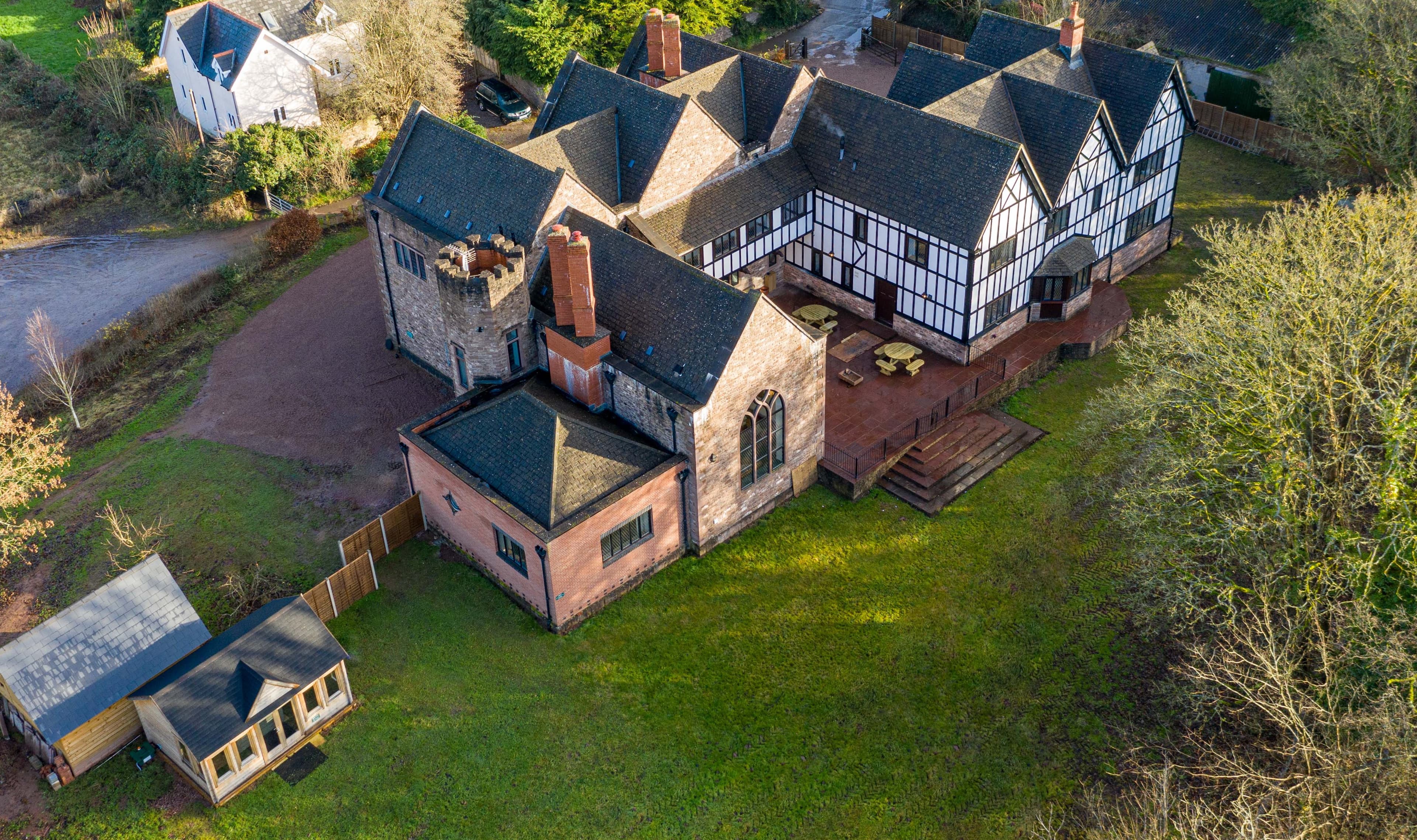 Aerial view of large brick manor house with multiple wings, chimneys, manicured grounds, and river nearby