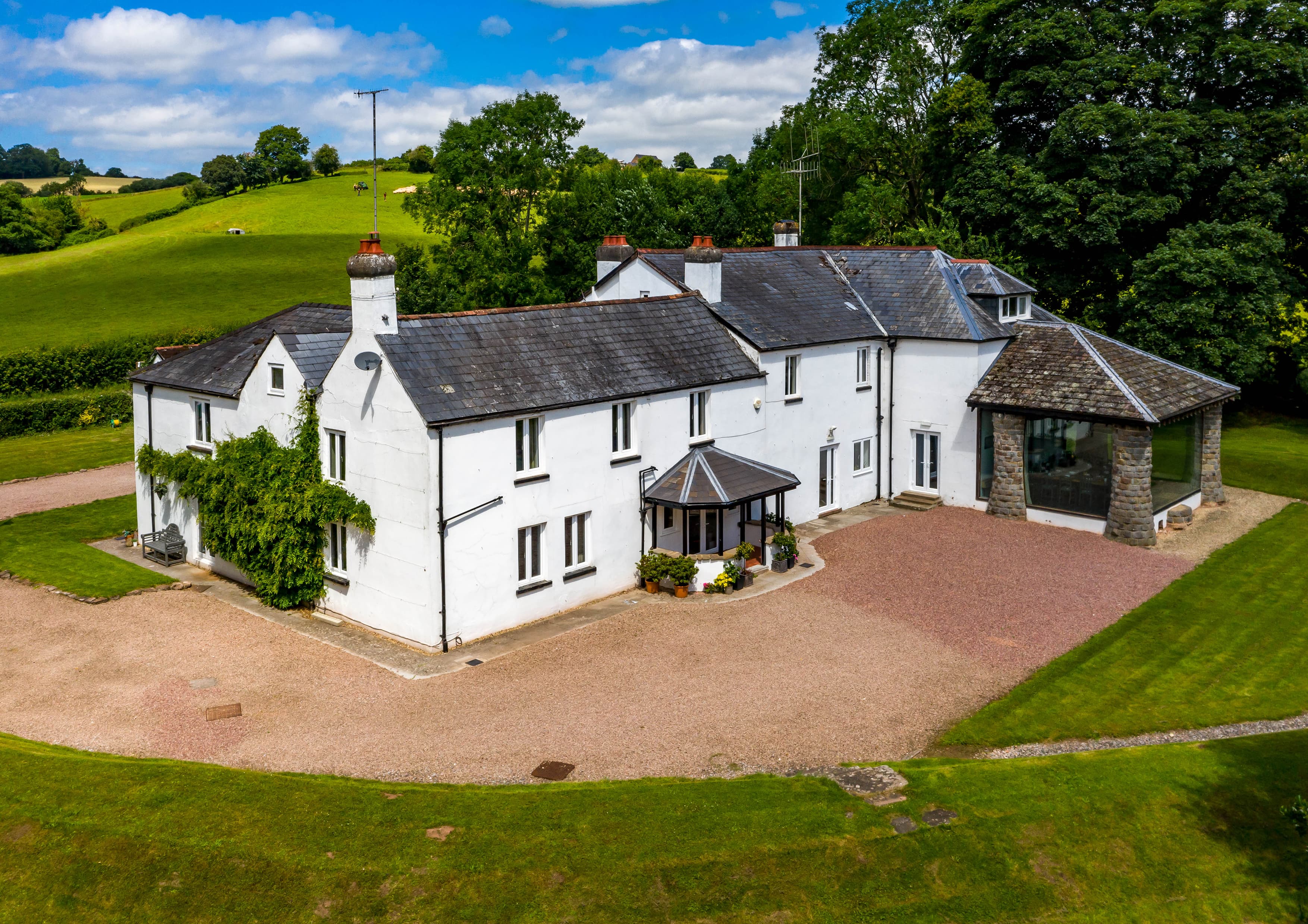Aerial view of white country house with slate roof, manicured grounds and countryside backdrop